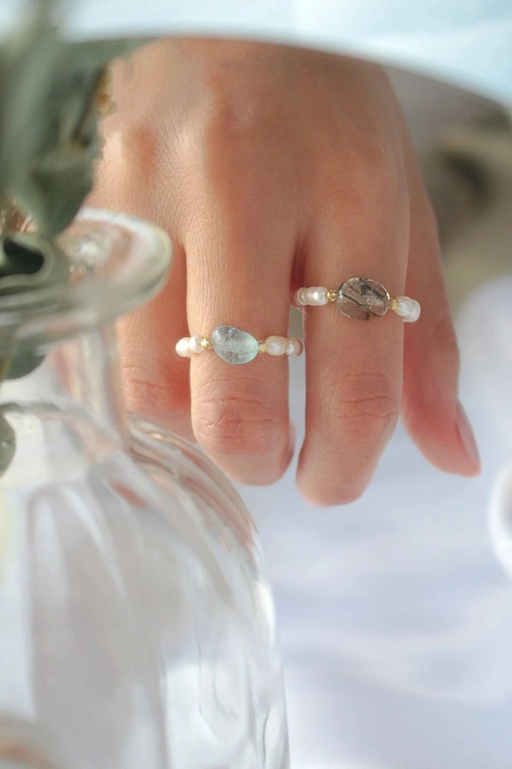Close-up of a hand wearing two rings with gemstones on a blurred background