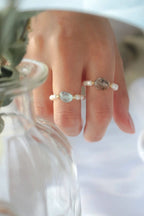 Close-up of a hand wearing two rings with gemstones on a blurred background