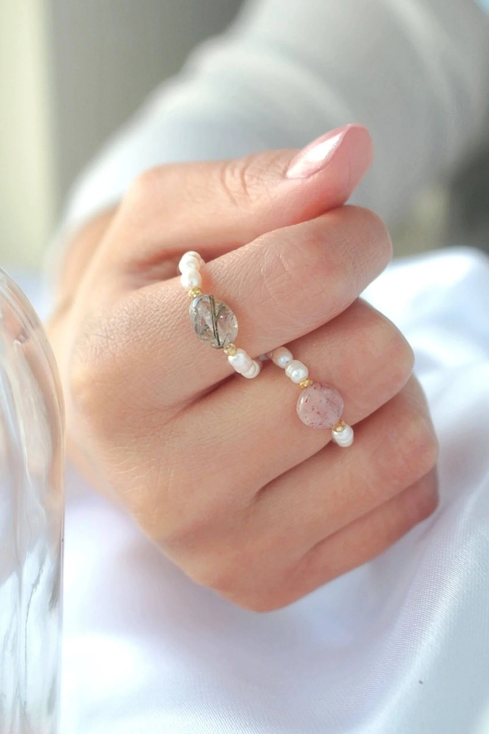 Close-up of a hand wearing multiple pearl and gemstone rings on a blurred background