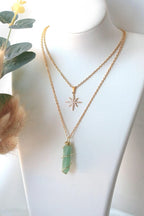 Mannequin wearing two gold necklaces with star and green crystal pendants.
