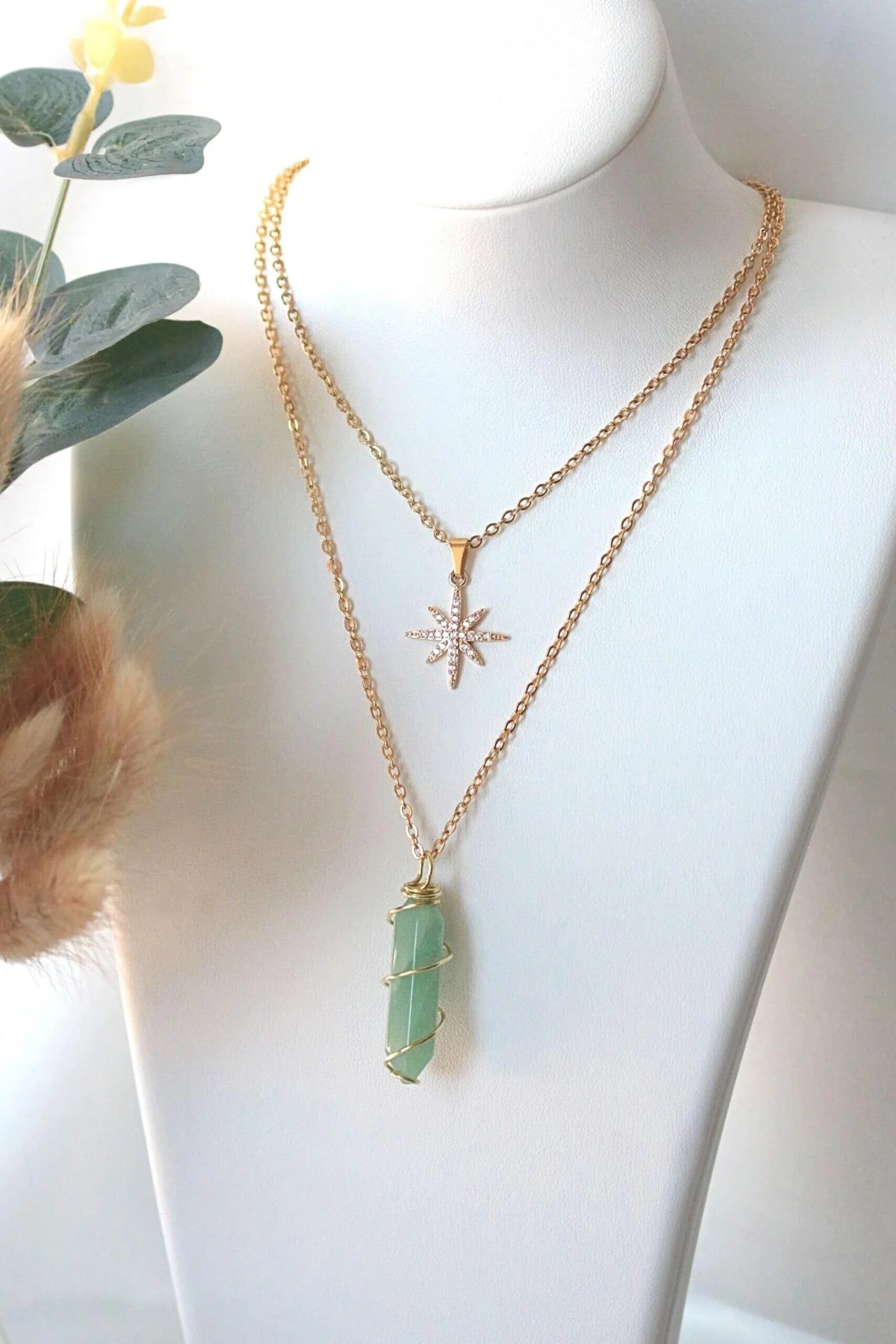 Mannequin wearing two gold necklaces with star and green crystal pendants.