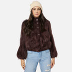 Woman wearing a brown faux fur jacket, light blue jeans, and a beige beanie on a white background