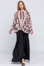 Woman wearing a patterned blouse and black pants on a white background