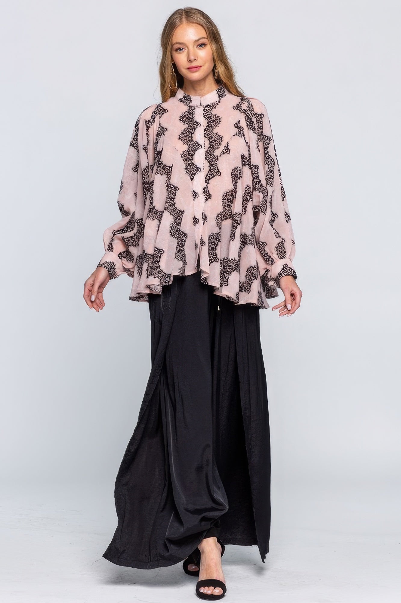 Woman wearing a patterned blouse and black pants on a white background