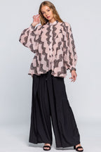 Woman wearing a pink blouse with black pattern and black wide-leg pants on a white background