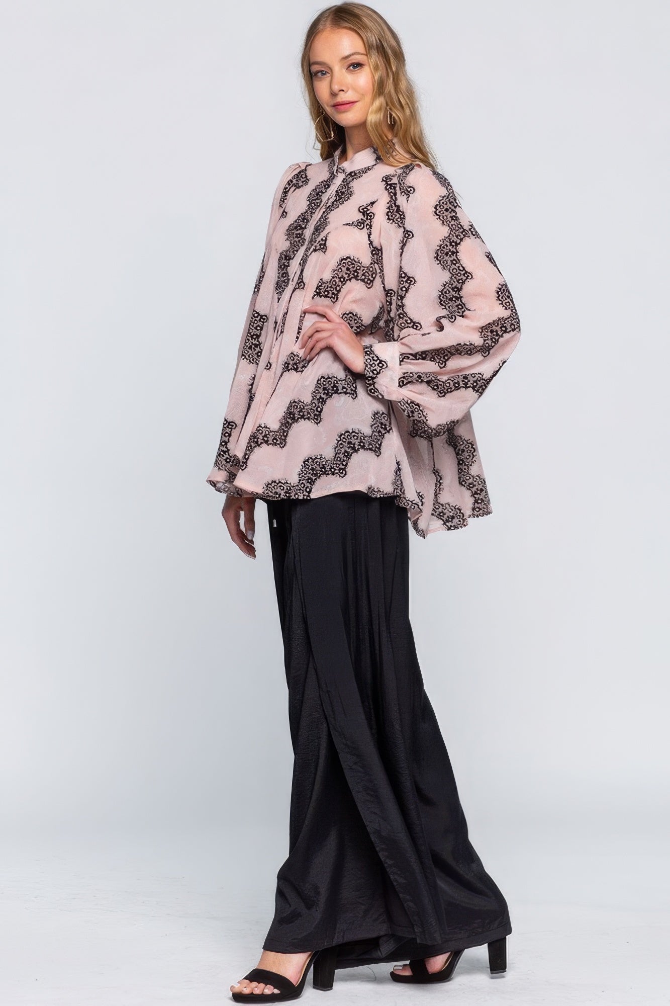 Woman wearing a pink patterned blouse and black pants on a white background