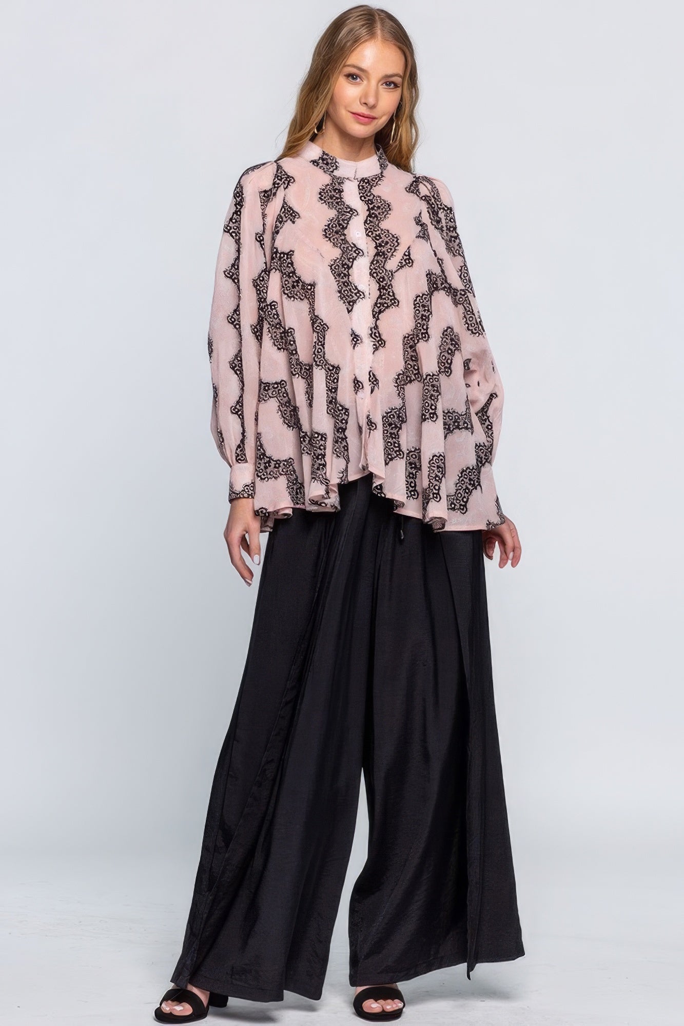 Woman wearing a patterned blouse and black pants on a white background