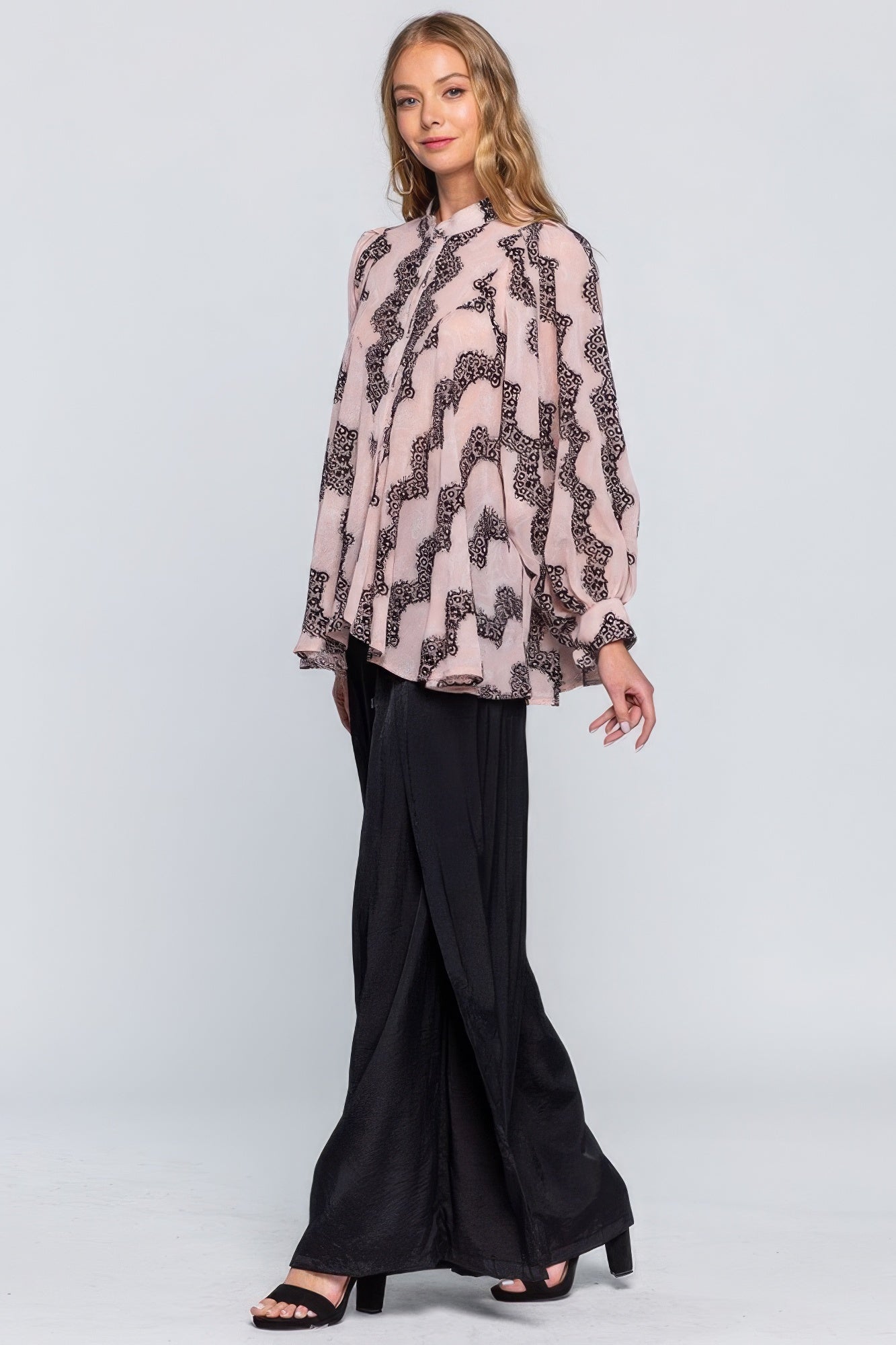 Woman wearing a patterned blouse and black pants on a white background
