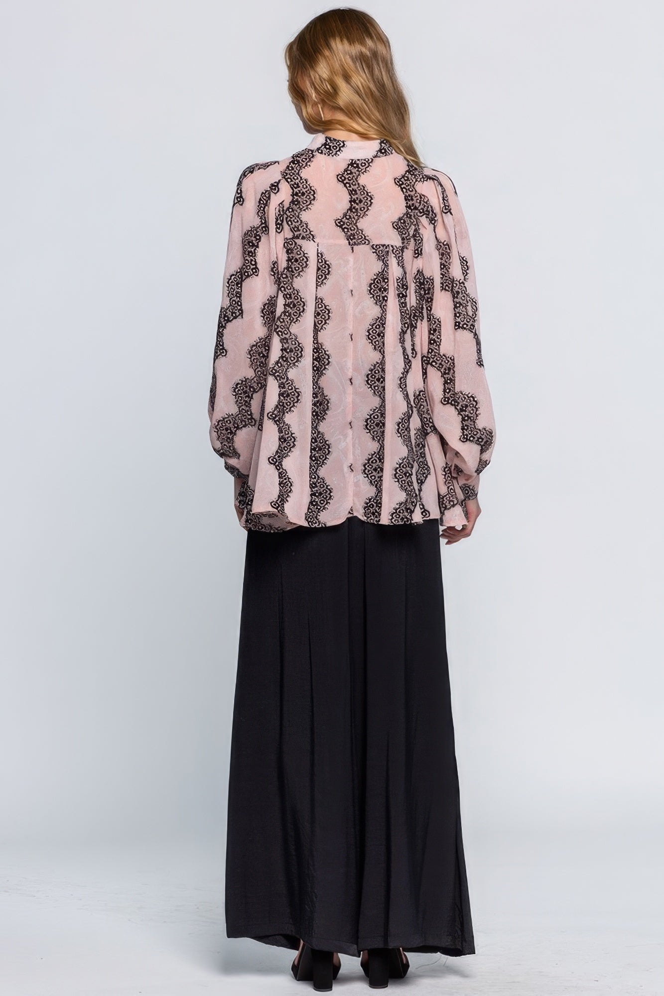 Woman wearing a pink patterned blouse and black pants on a white background