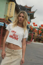 Woman wearing a white t-shirt with 'My Own Muse' text in an outdoor setting with traditional architecture and decorations.
