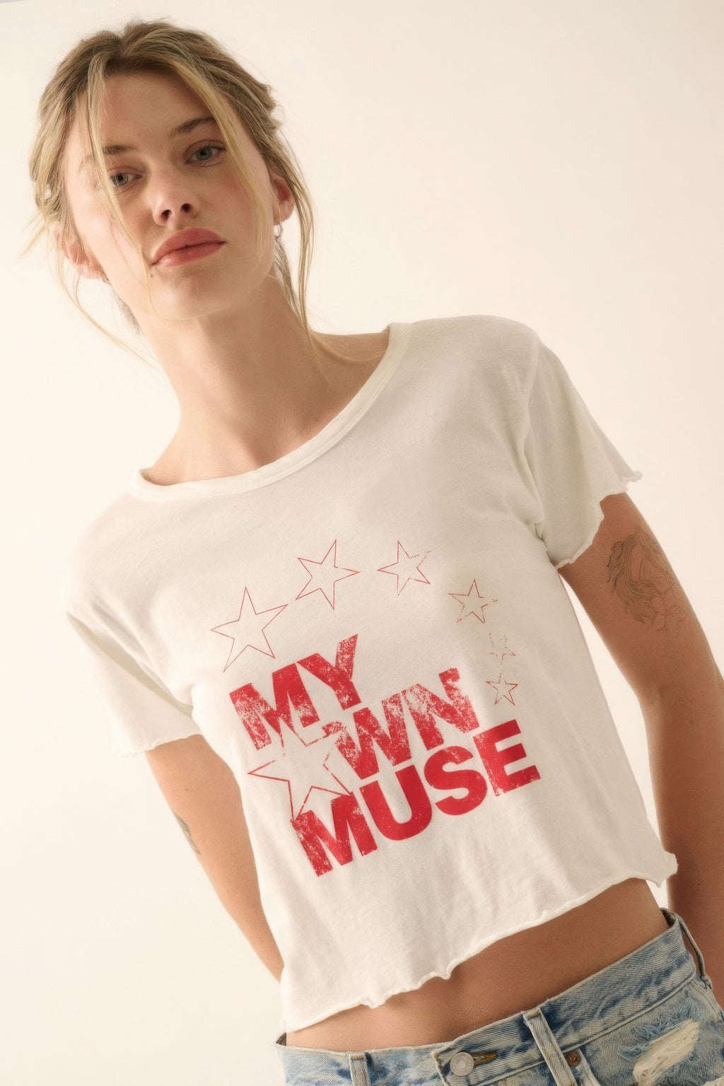 Woman wearing a white t-shirt with 'My Own Muse' text and star designs.