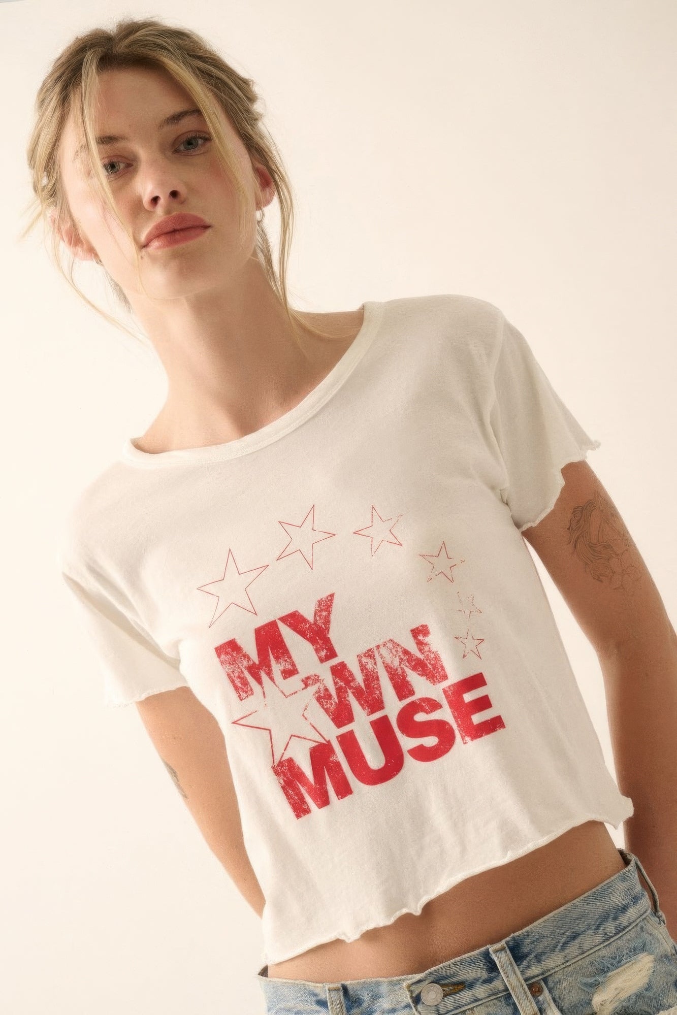 Woman wearing a white t-shirt with 'My Own Muse' text and star designs.