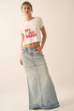 Woman wearing a white crop top with text and light blue jeans on a plain background