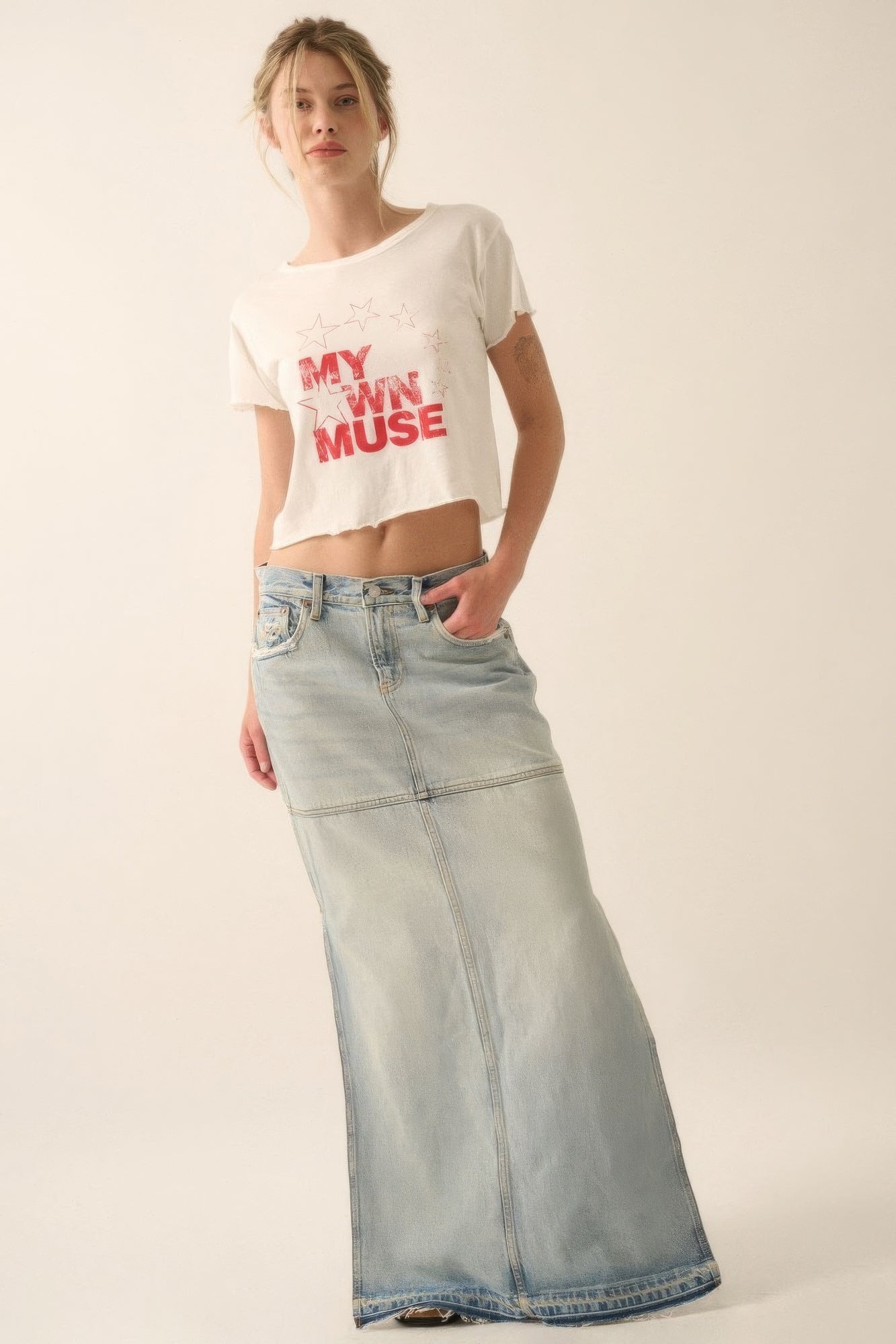 Woman wearing a white crop top with text and light blue jeans on a plain background