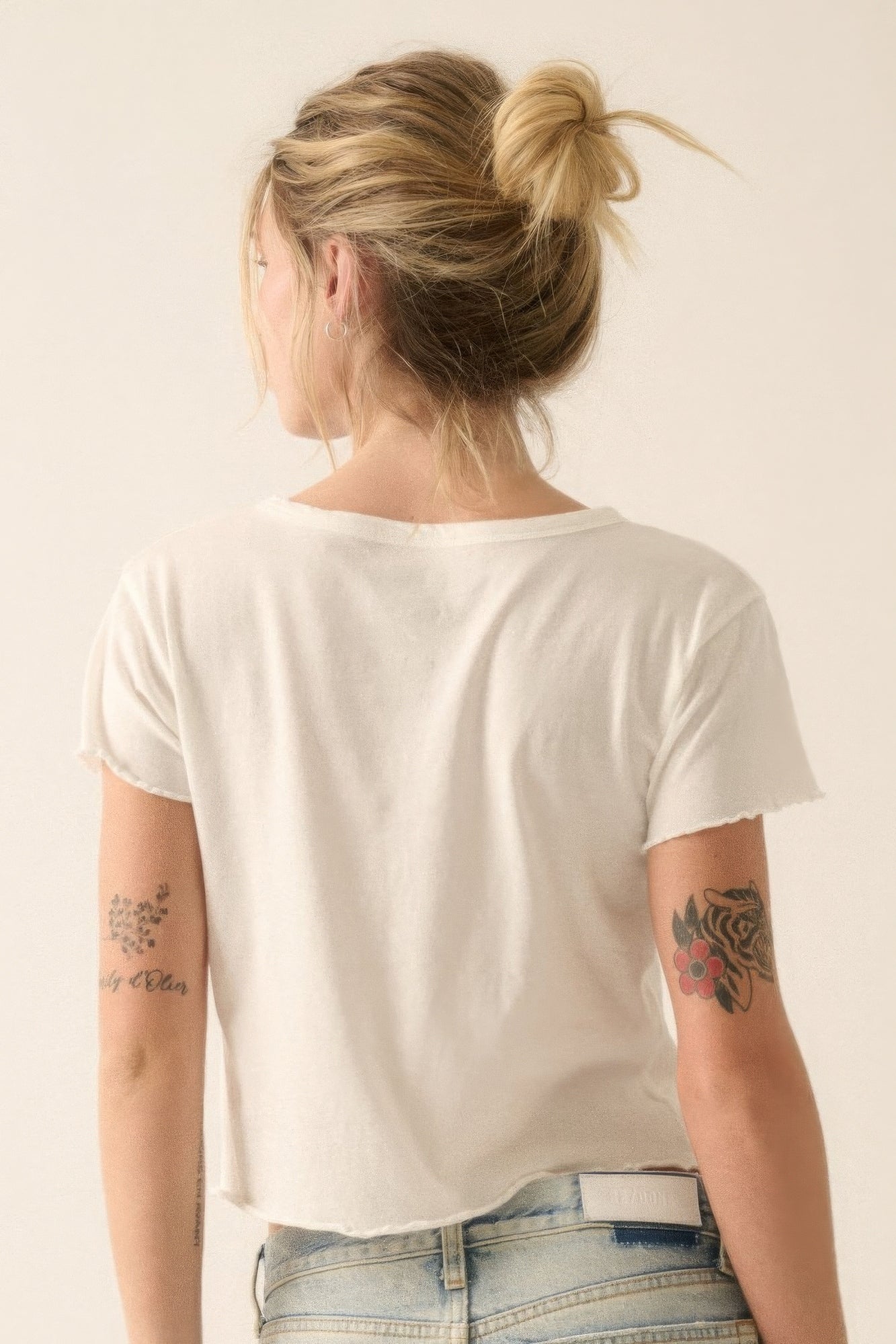 Person wearing a plain white t-shirt and blue jeans with tattoos on arms against a light background