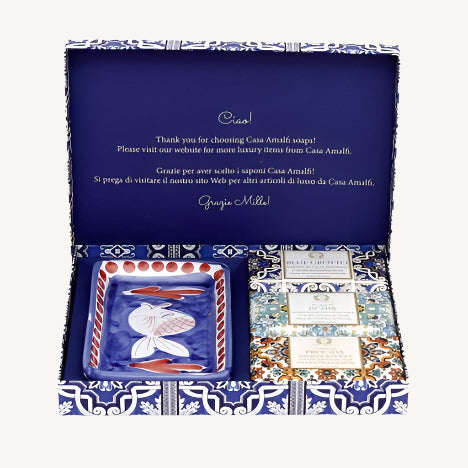 "Casa Amalfi Blue Maiolica Gift Box with two vegan body soaps—Blue Grotto Acqua Marine and Sunset in Procida Honey & Vanilla—and one Ischia Water Jasmine & Chamomile body scrub soap, plus a hand-painted ceramic soap dish from Vietri Sul Mare, all inspired by the Amalfi Coast and beautifully presented in a blue maiolica design."
