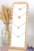 Necklace with stones on a wooden stand next to a vase with wheat and crystals.