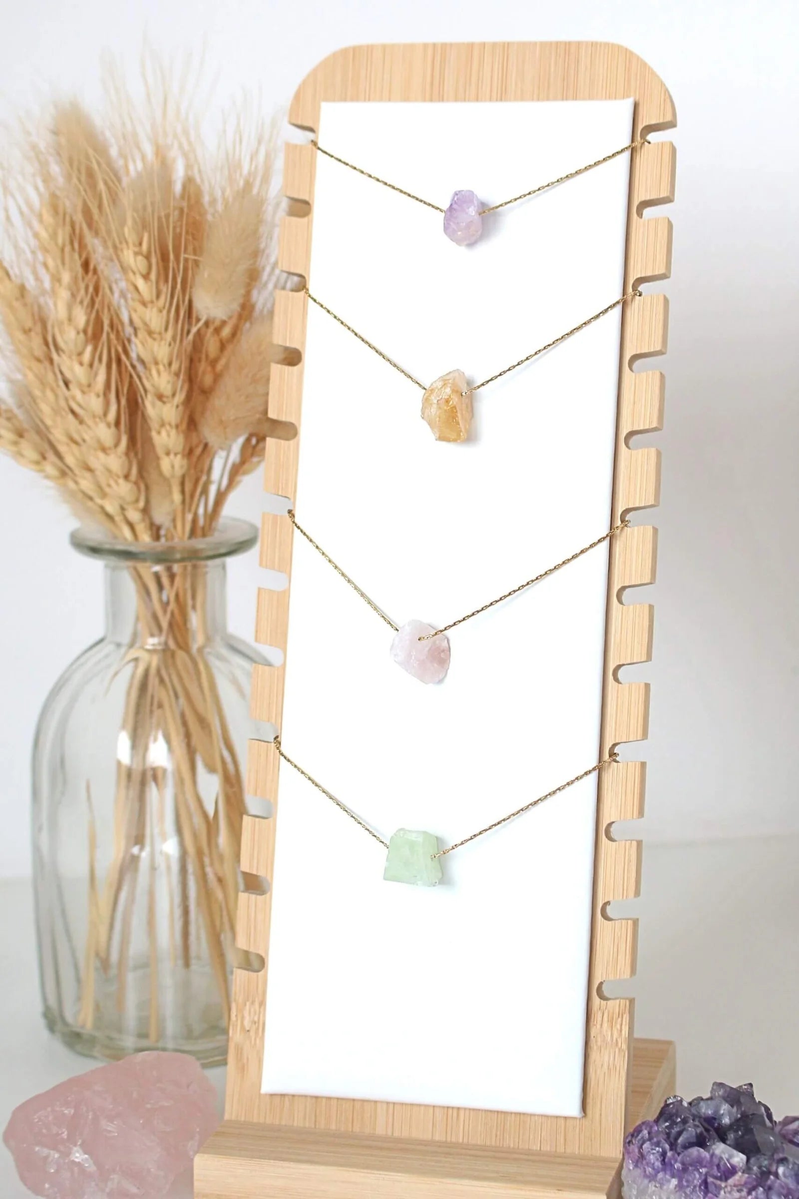 Necklace with stones on a wooden stand next to a vase with wheat and crystals.