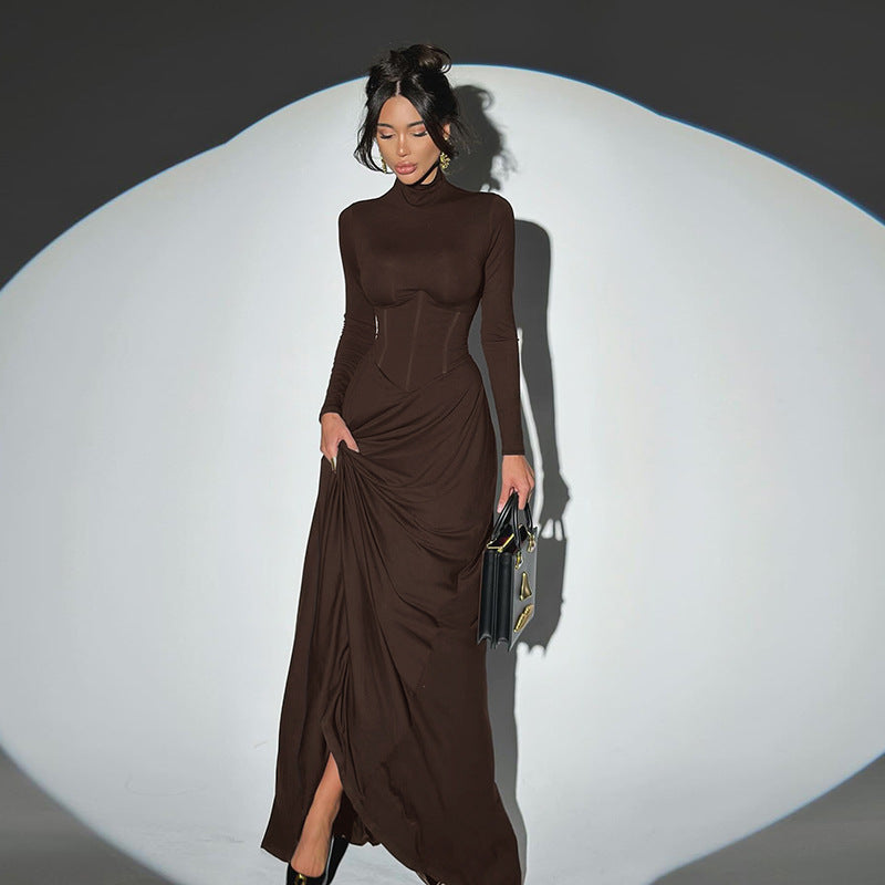 Woman wearing a brown dress with a high slit, holding a clutch against a white background