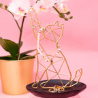 Gold geometric jewelry holder with jewelry on a pink background