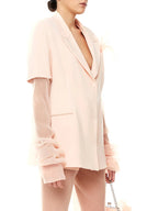 Woman wearing a light pink blazer with ruffled sleeves on a white background