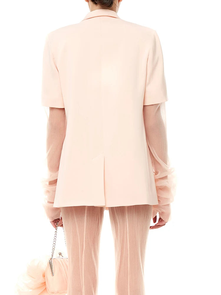 Person wearing a light pink suit with sheer pants on a white background