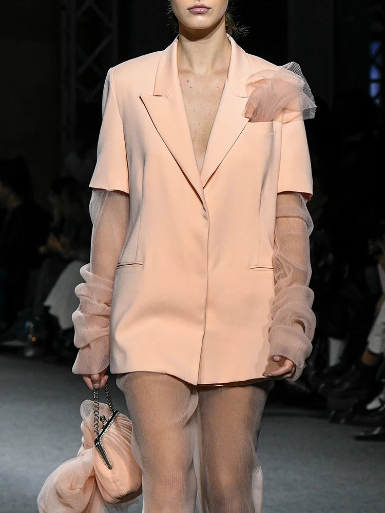 Model wearing a light pink outfit with sheer sleeves on a runway.