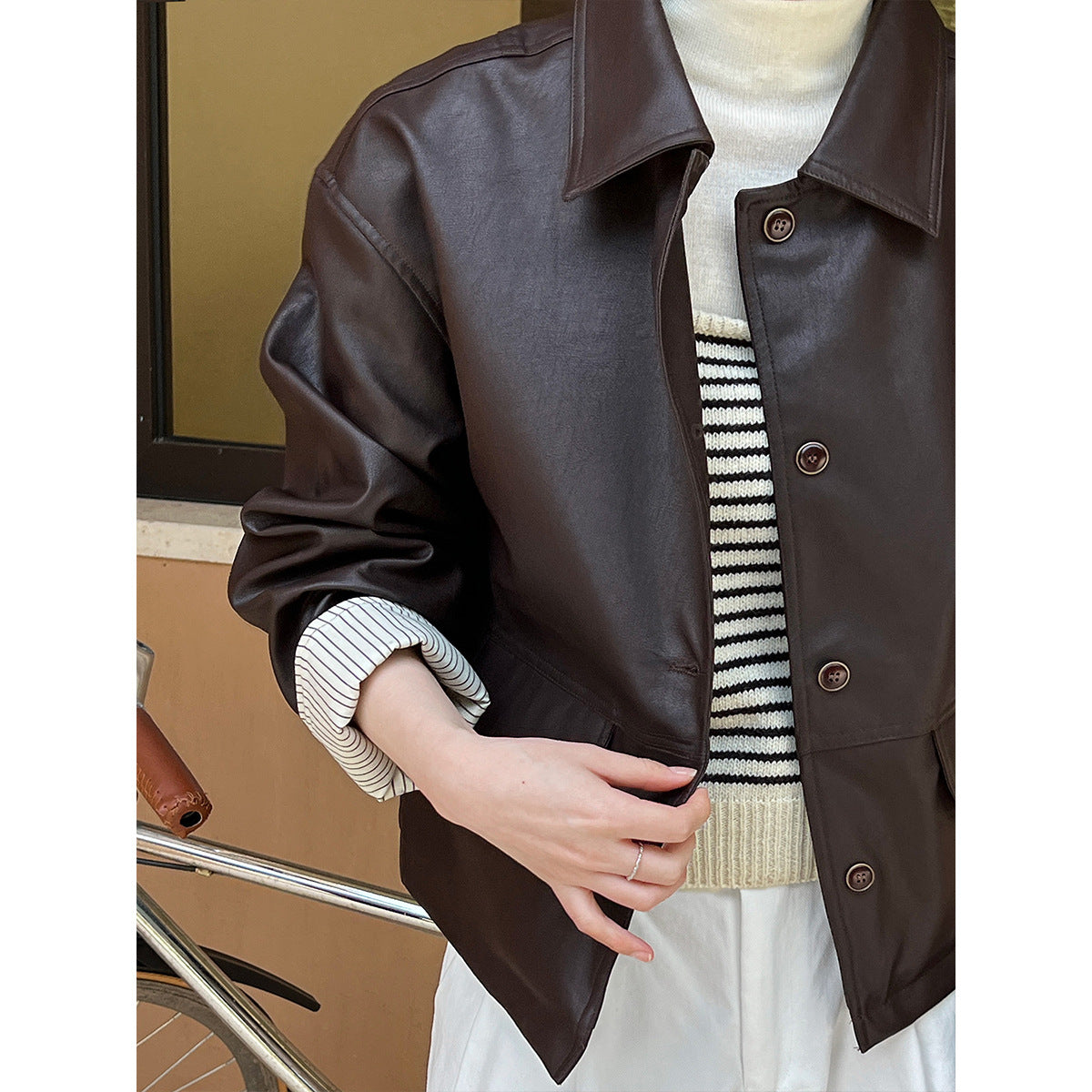 Brown leather jacket worn by a person with a striped sweater underneath, on a neutral background.