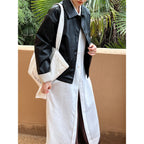 Person wearing a black leather jacket over a white shirt and pants, holding a beige bag with text.