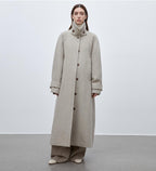 Person wearing a long beige coat against a plain background