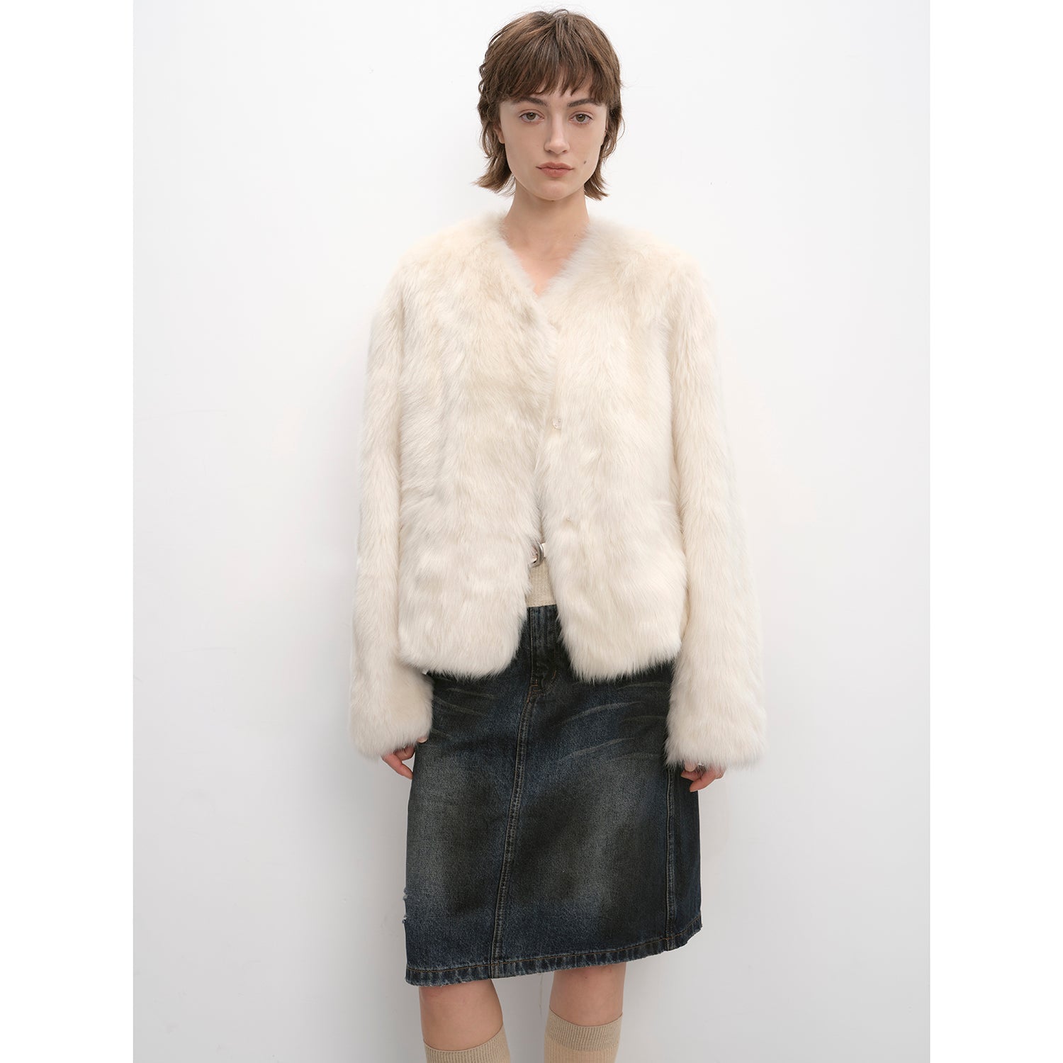 Woman wearing a white fur coat and denim skirt against a white background