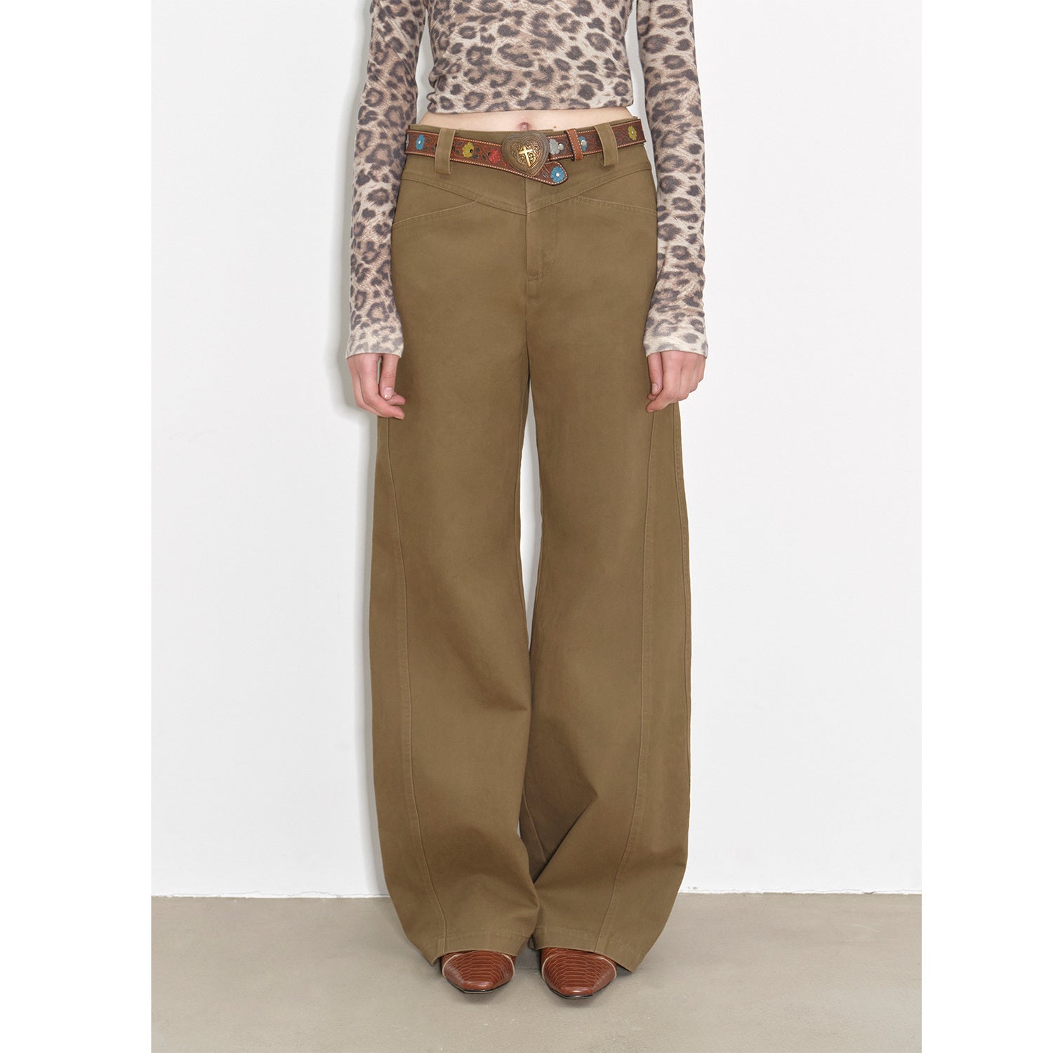 Person wearing brown wide-leg pants with a patterned top on a white background