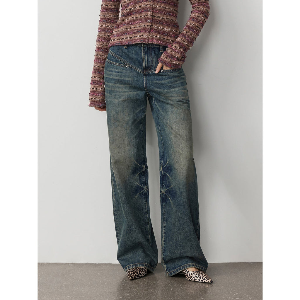 Person wearing blue jeans and a patterned top against a plain background