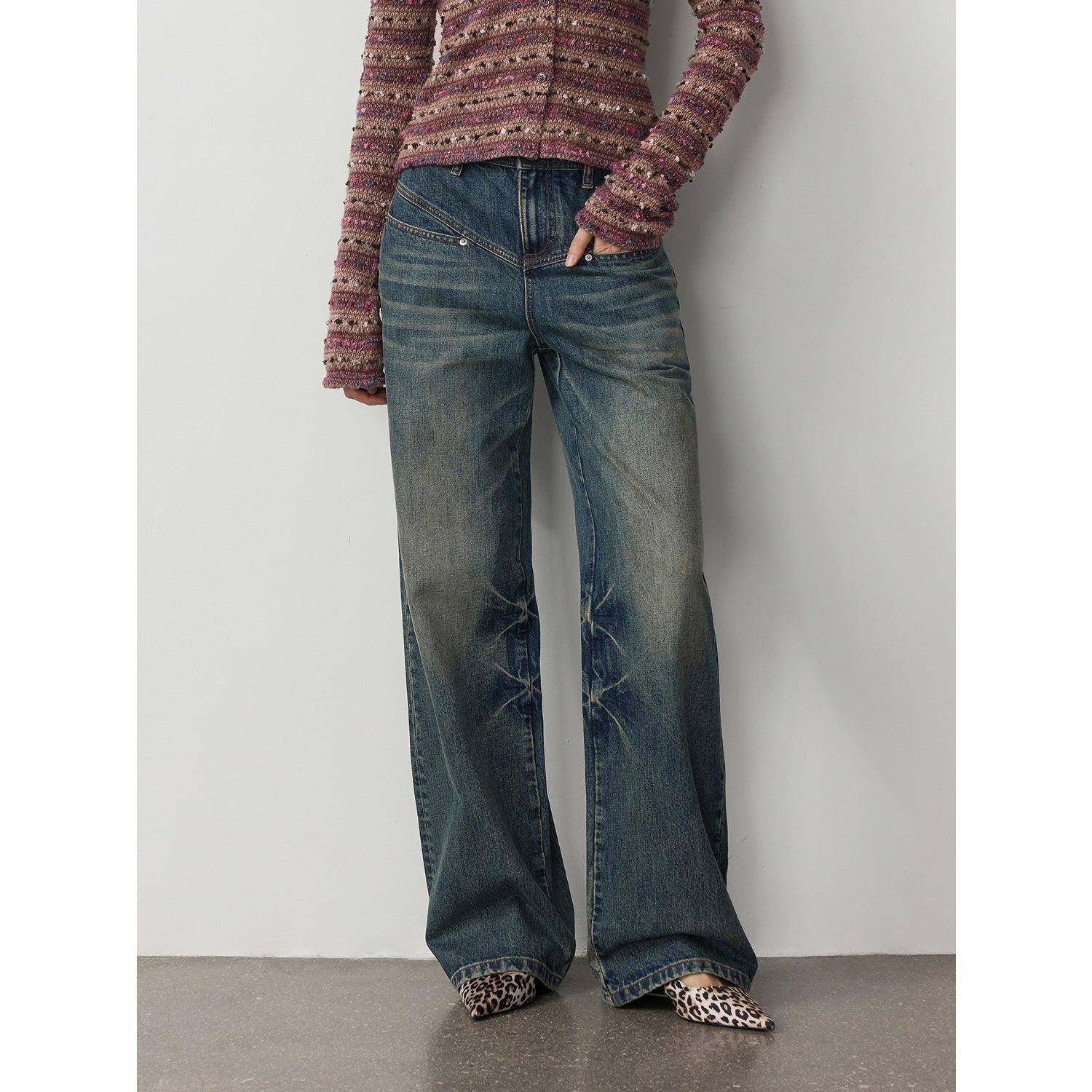 Person wearing blue jeans and a patterned top against a plain background