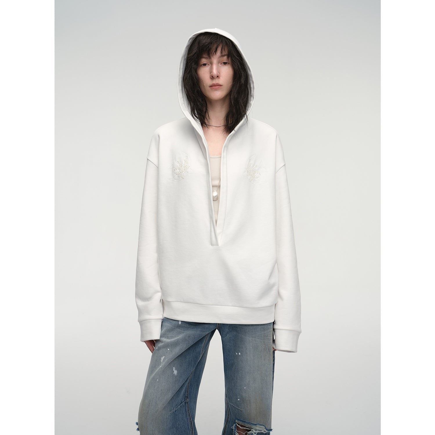 Person wearing a white hoodie with a zipper on a plain background