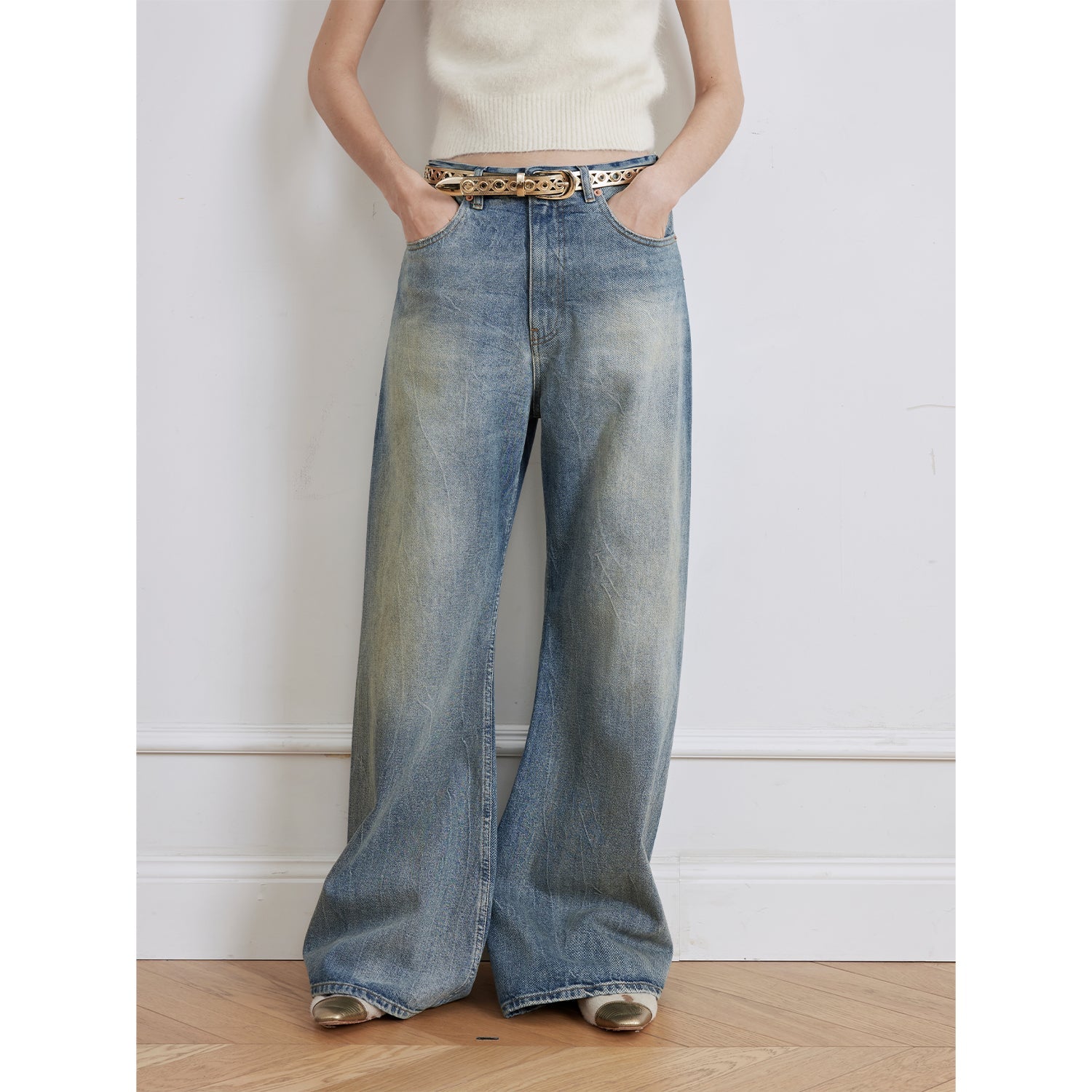 Person wearing wide-leg jeans with a gold belt against a white wall.