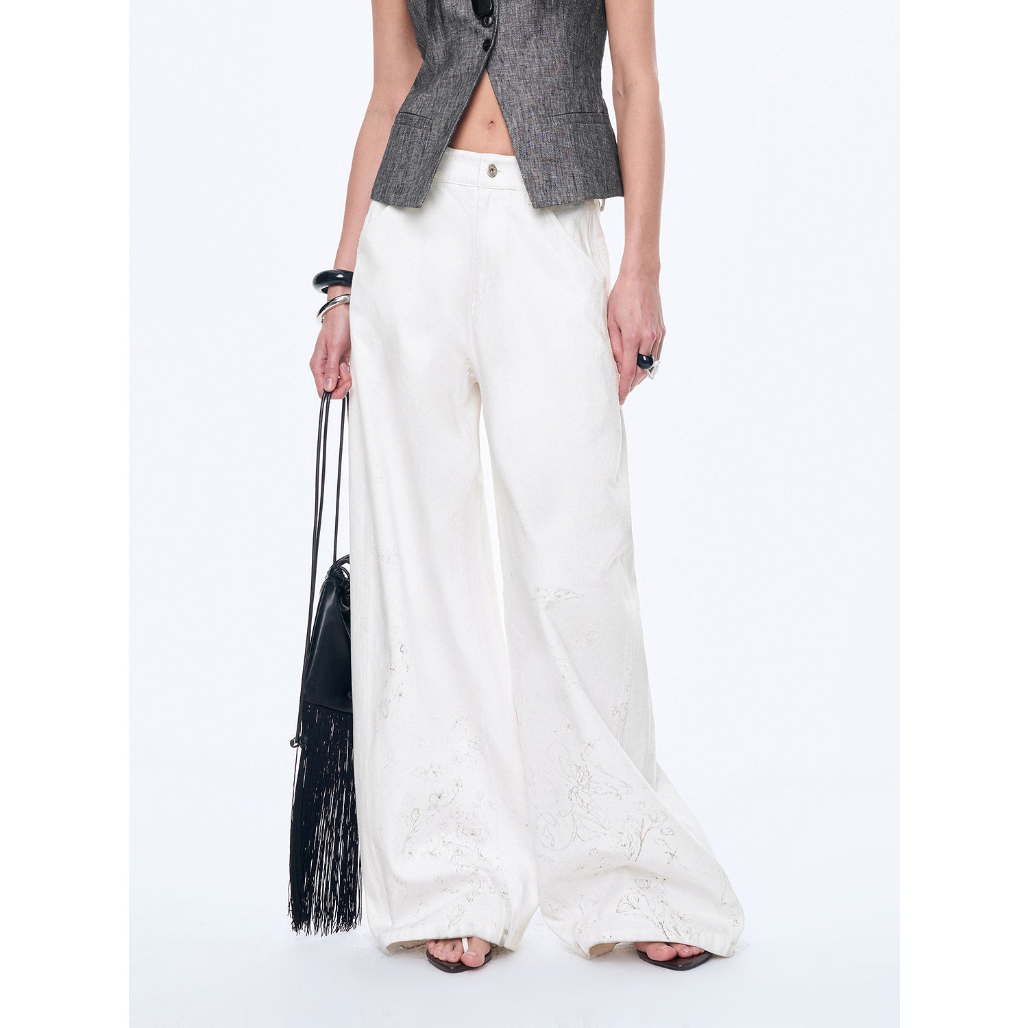 Person wearing white pants and a gray vest holding a black handbag on a white background