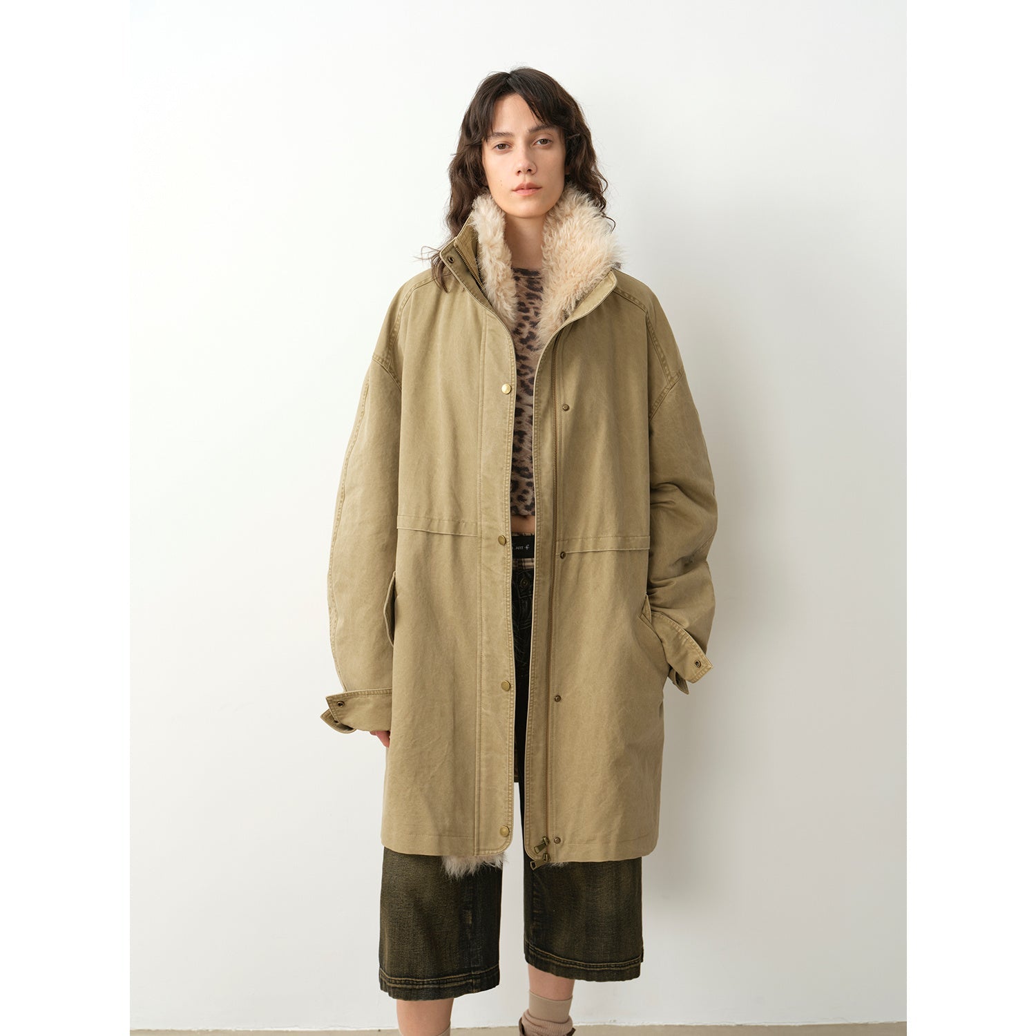 Person wearing a long beige coat with fur trim on a white background