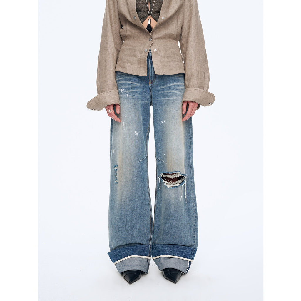 Person wearing a beige blazer and distressed blue jeans on a white background