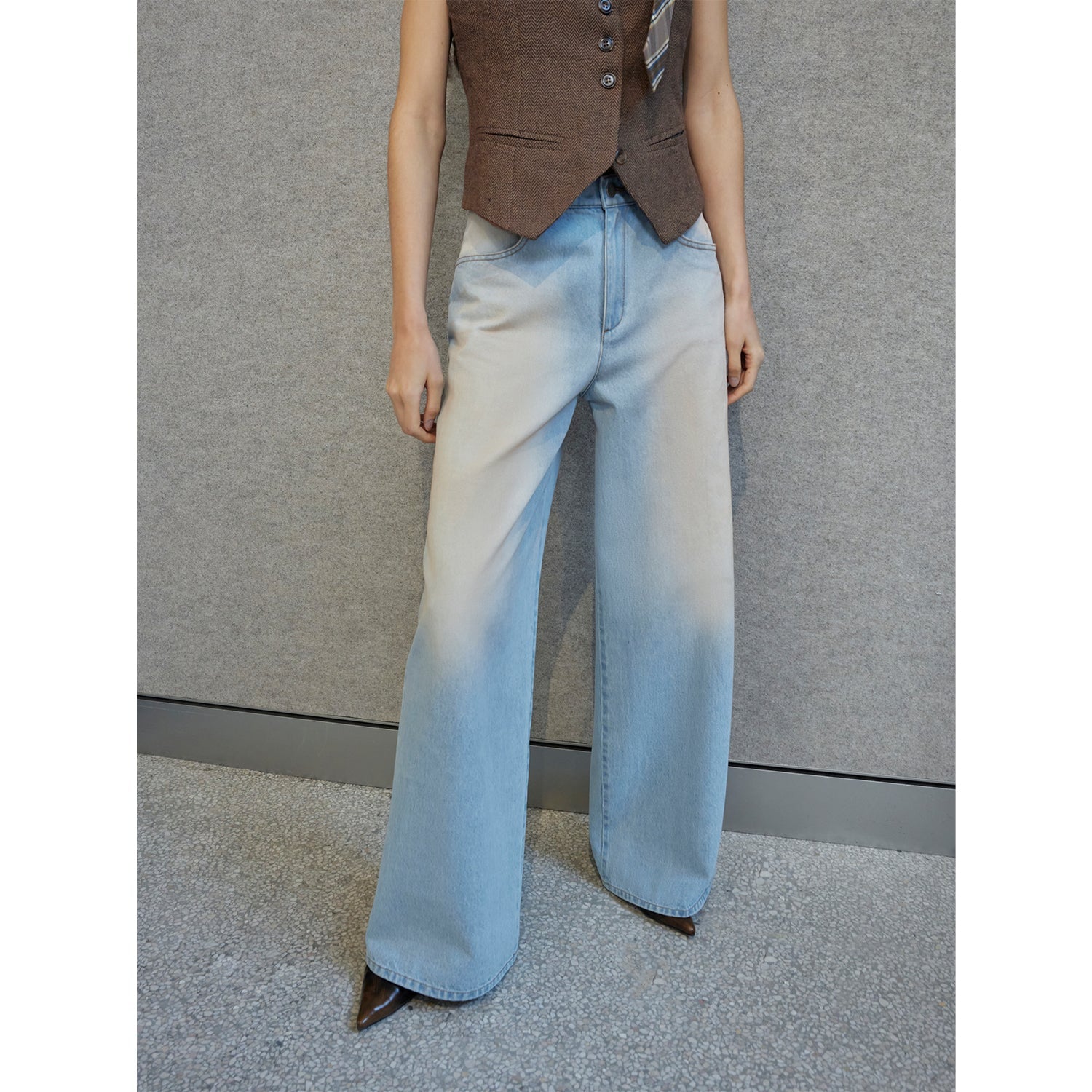 Person wearing light blue wide-leg jeans and a brown vest against a gray background