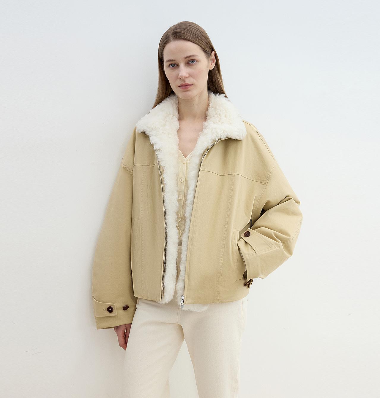 Woman wearing a beige jacket with white shearling lining on a plain background