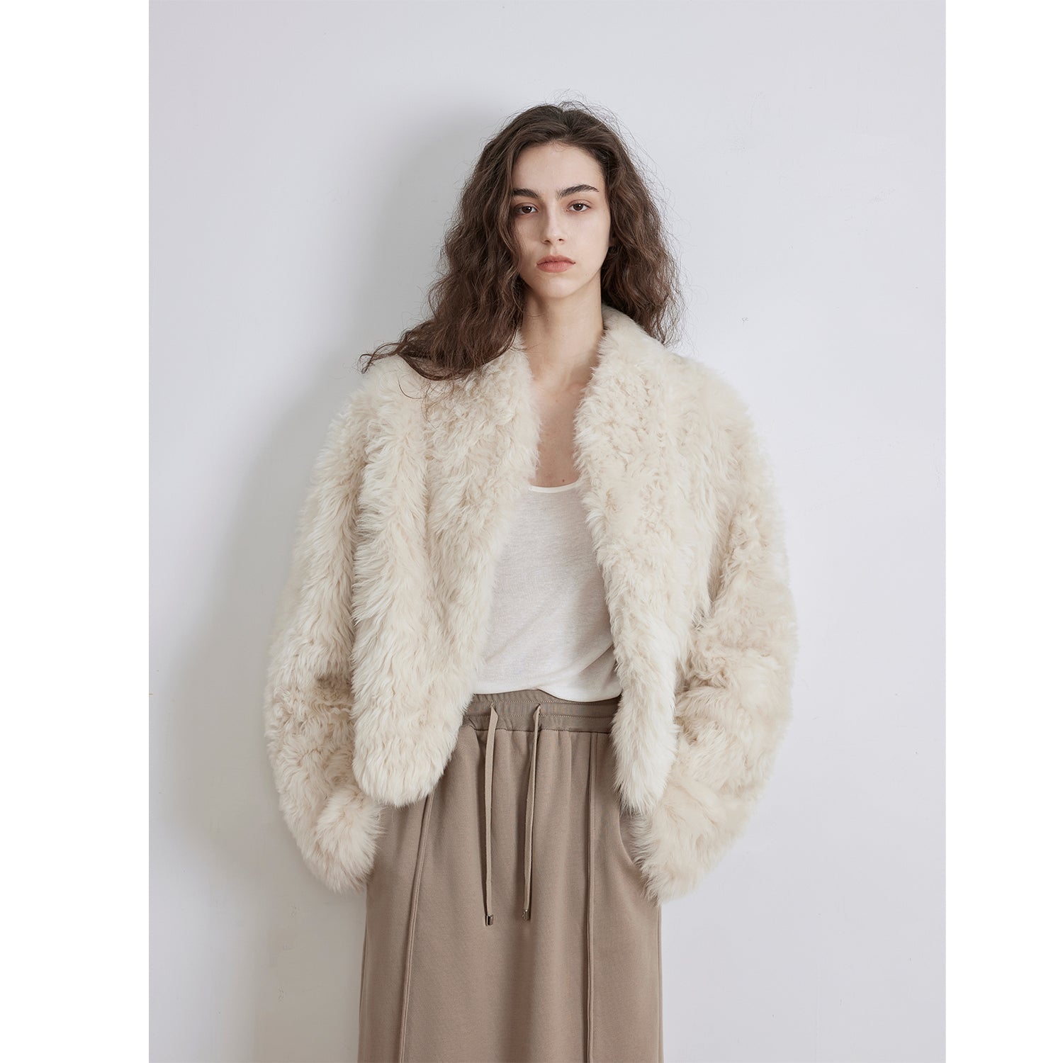 Woman wearing a fluffy white jacket over a white shirt and beige pants on a light gray background