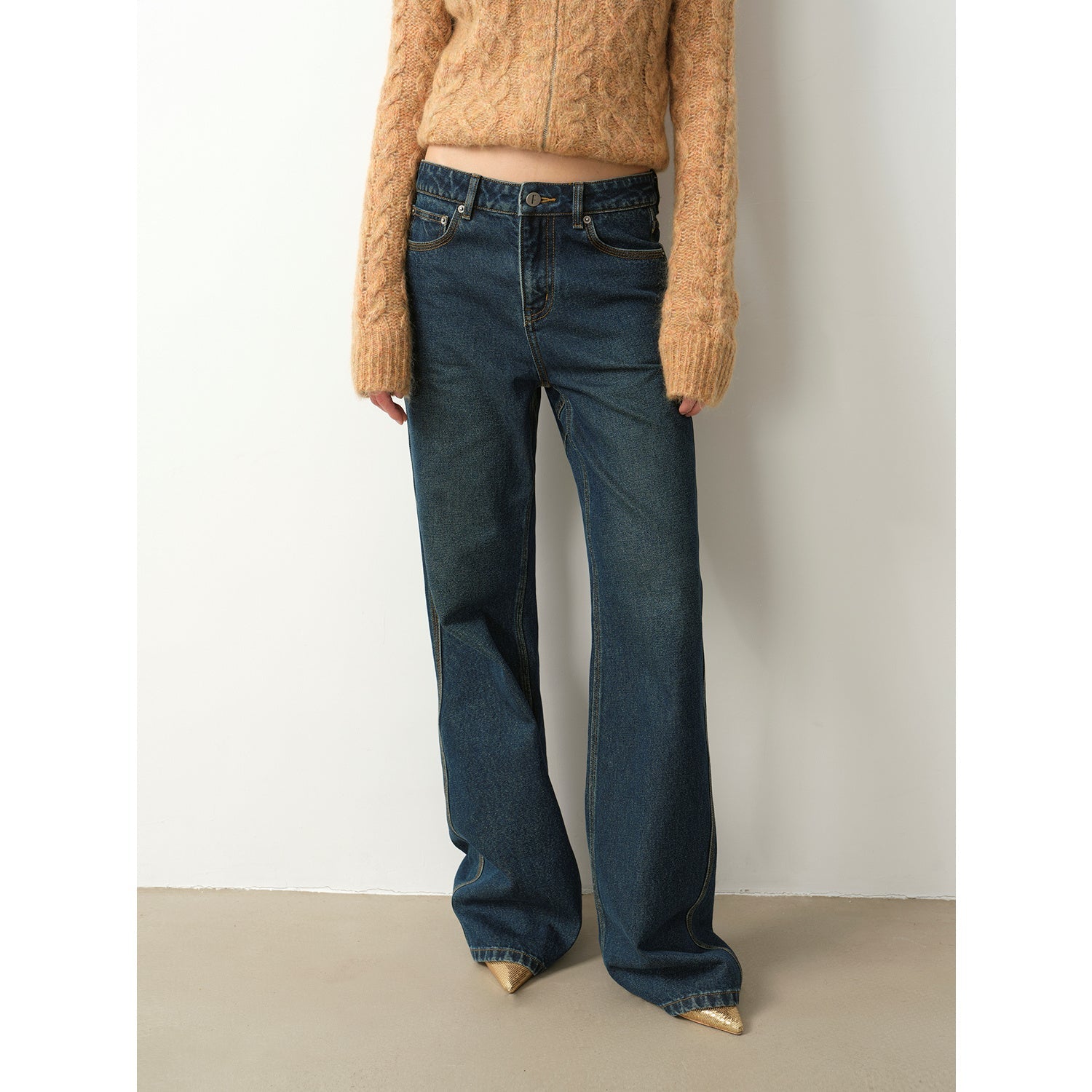 Person wearing blue jeans and a beige sweater against a plain background