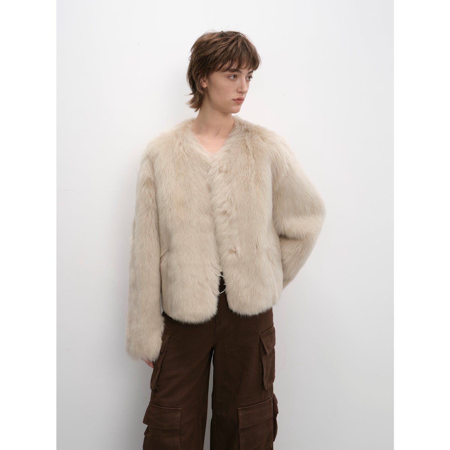 Person wearing a beige fur coat against a white background