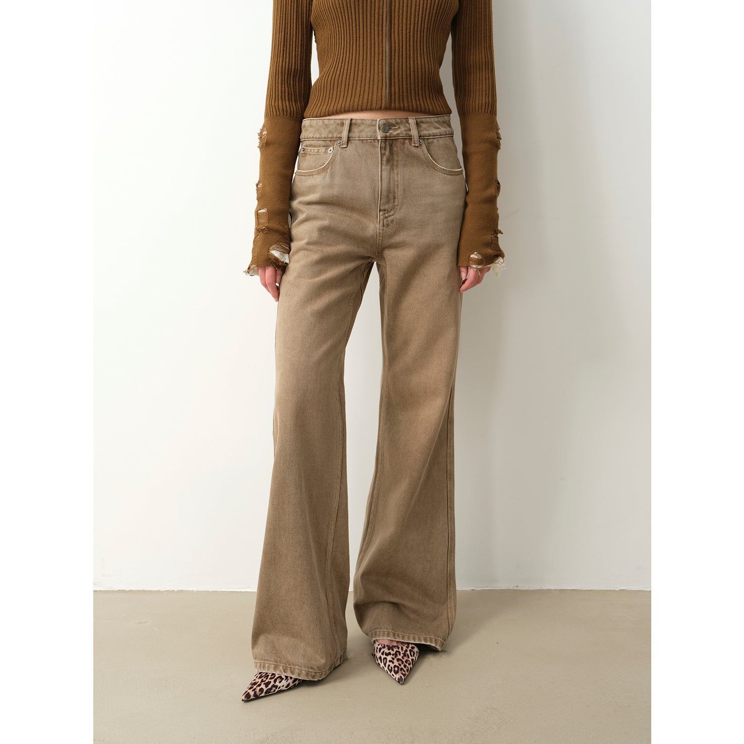Person wearing a brown ribbed sweater and beige flared pants on a plain background