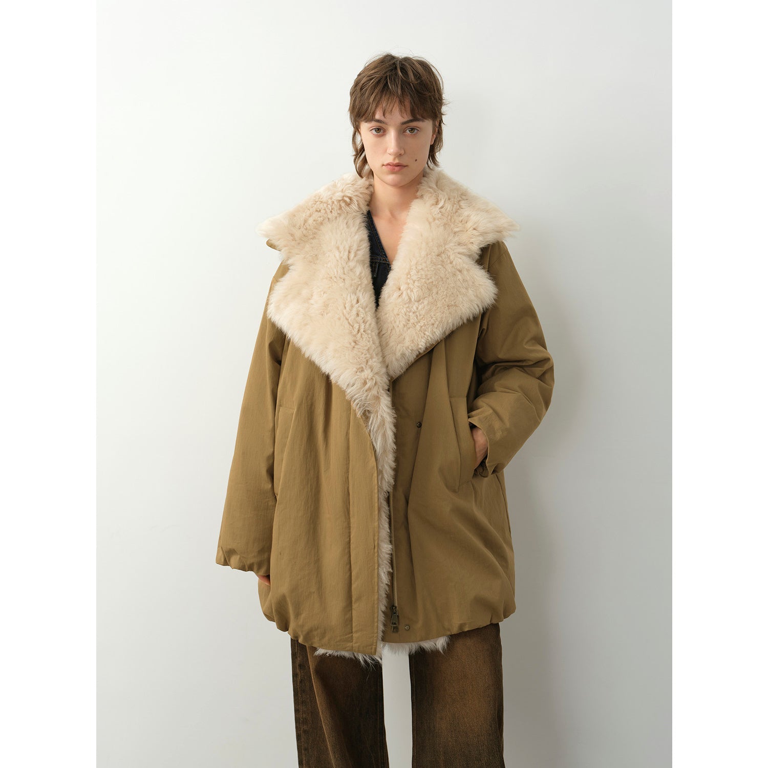 Person wearing a brown coat with a fur-lined hood against a white background