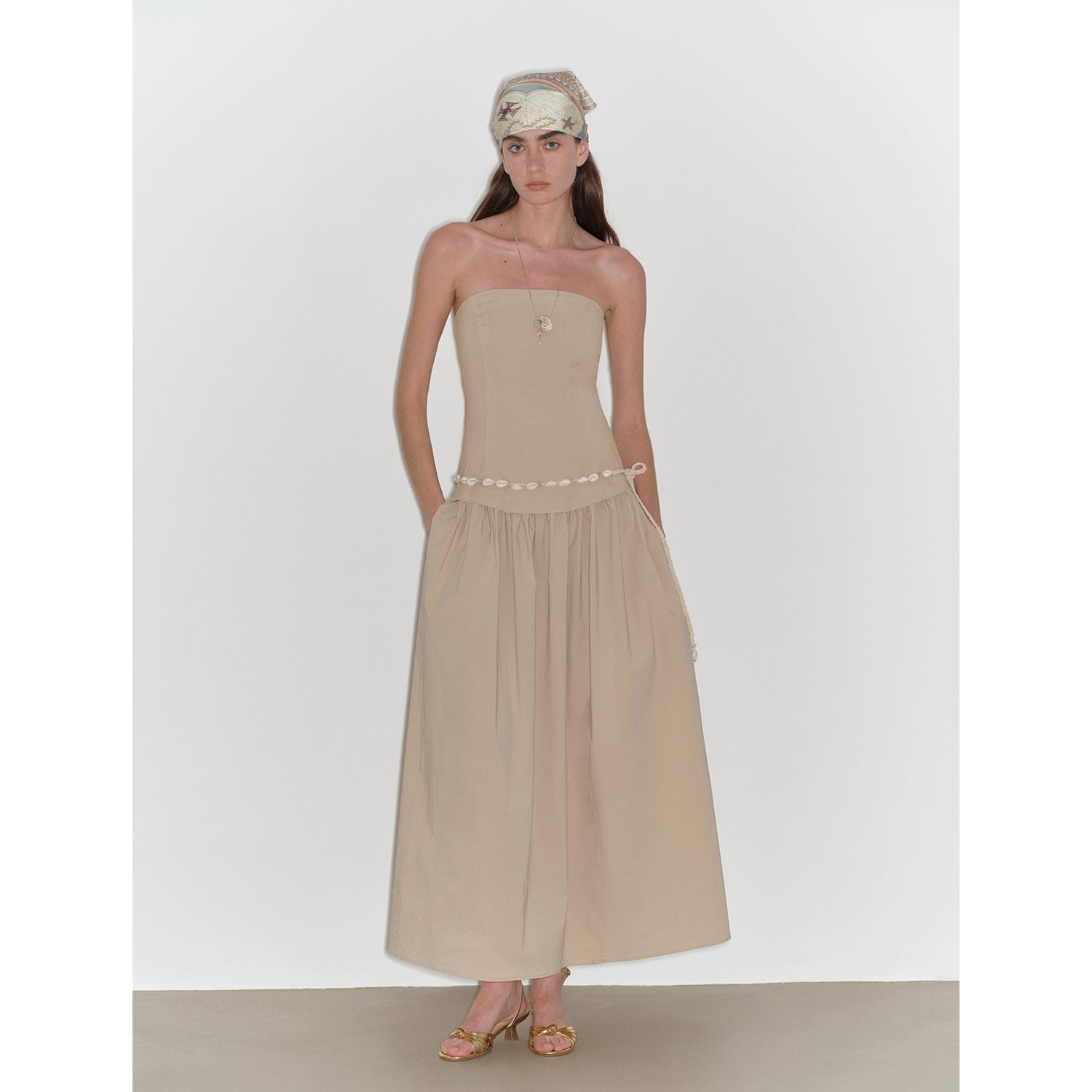 Woman wearing a beige strapless dress with a white headband on a white background