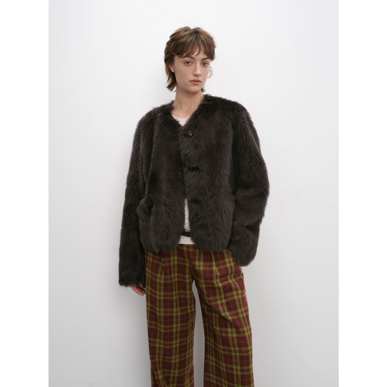 Person wearing a dark brown fuzzy jacket and plaid pants against a white background