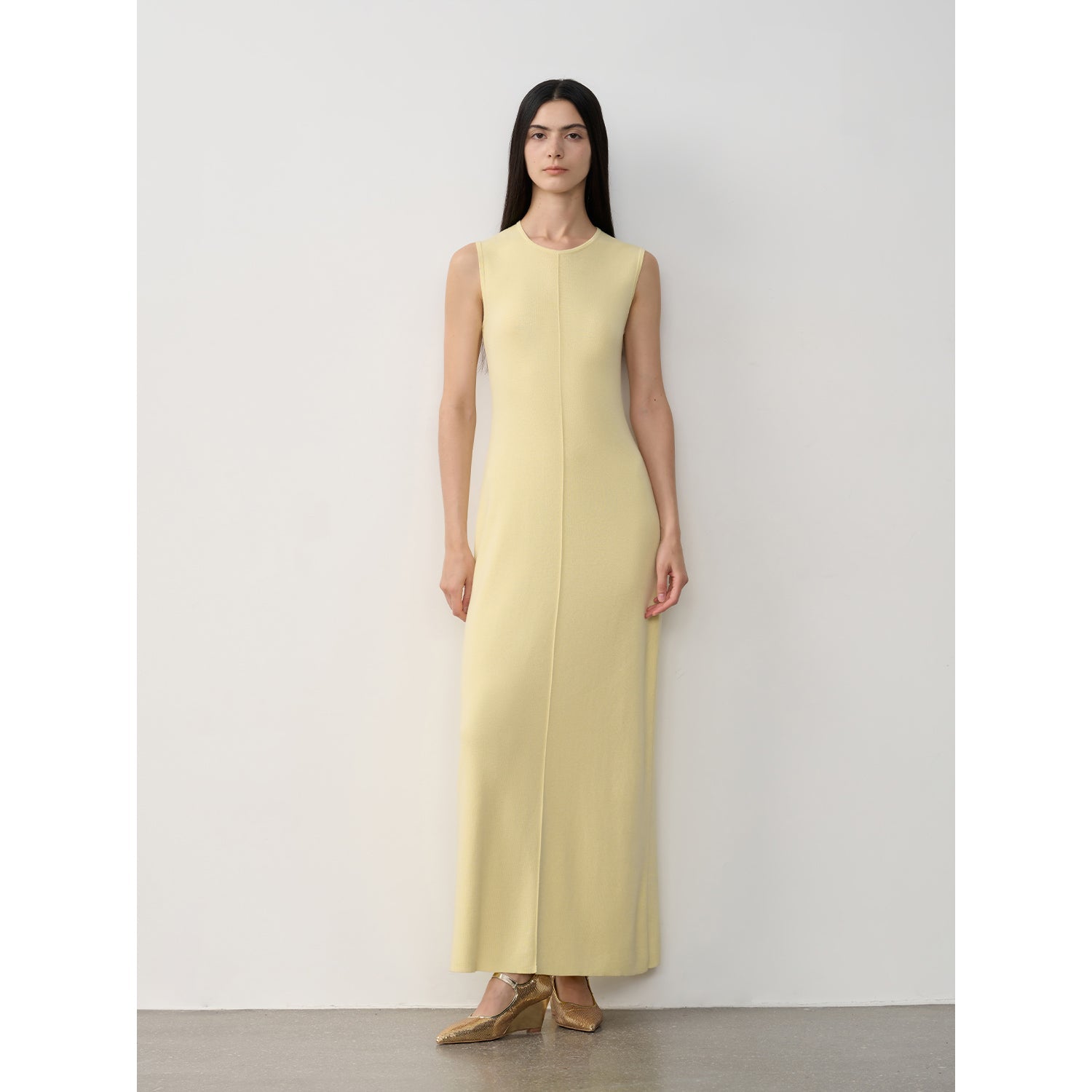 Woman wearing a light yellow sleeveless dress against a white background