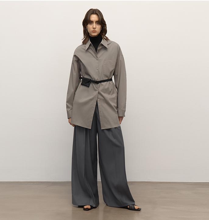 Person wearing a beige trench coat and gray pants against a white background